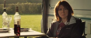 Movie still from “Sightseers” (2012), directed by Ben Wheatley – A woman sitting at a table in front of an rv; Medium shot, Over the shoulder angle