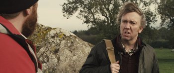 Movie still from “Sightseers” (2012), directed by Ben Wheatley – A woman standing next to a rock in a wooded area; Close Up shot, Over the shoulder angle