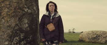 Movie still from “Sightseers” (2012), directed by Ben Wheatley – A woman standing next to a tree in a grassy field; Medium shot, Low angle