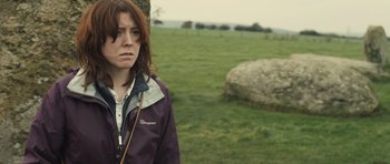 Movie still from “Sightseers” (2012), directed by Ben Wheatley – A woman standing in a field near a tree; Close Up shot, Over the shoulder angle