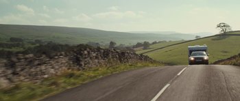 Movie still from “Sightseers” (2012), directed by Ben Wheatley – A view from a car of a country road with a stone wall on the side of the road; Extreme Wide shot, Low angle