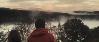 Movie still from “Sightseers” (2012), directed by Ben Wheatley – A man in a red jacket looking out over a body of water; Medium shot, Low angle