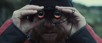 Movie still from “Sightseers” (2012), directed by Ben Wheatley – A man with a beard looking through a pair of binoculars; Extreme Close Up shot, Low angle