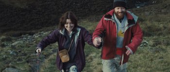 Movie still from “Sightseers” (2012), directed by Ben Wheatley – A man and a woman holding hands while walking through a field; Medium shot, Over the shoulder angle