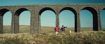 Movie still from “Sightseers” (2012), directed by Ben Wheatley – Two people and a dog walking under a stone arch; Extreme Wide shot, Low angle