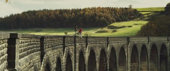 Movie still from “Sightseers” (2012), directed by Ben Wheatley – Two people are standing on a bridge over a river; Extreme Wide shot, Low angle