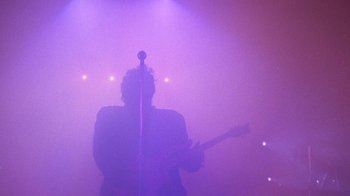 Movie still from “Sign 'o' the Times” (1987), directed by Albert Magnoli – A person holding a guitar in front of a microphone; Wide shot, Low angle