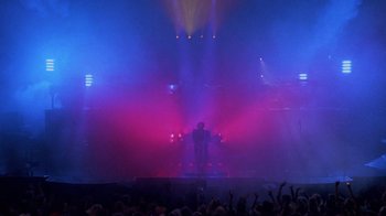 Movie still from “Sign 'o' the Times” (1987), directed by Albert Magnoli – A man standing on a stage in front of a crowd of onlookers; Extreme Wide shot, Low angle