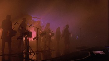 Movie still from “Sign 'o' the Times” (1987), directed by Albert Magnoli – A group of people standing in front of microphones in a room; Wide shot, Low angle