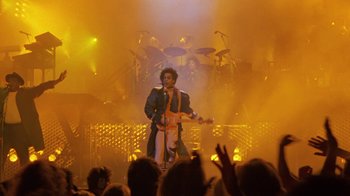 Movie still from “Sign 'o' the Times” (1987), directed by Albert Magnoli – A man with a guitar on stage in front of an audience; Wide shot, Low angle