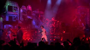 Movie still from “Sign 'o' the Times” (1987), directed by Albert Magnoli – A man is singing on stage in front of an audience; Wide shot, Low angle