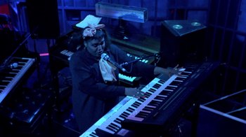 Movie still from “Sign 'o' the Times” (1987), directed by Albert Magnoli – A person playing a keyboard in a dark room; Medium shot, High angle