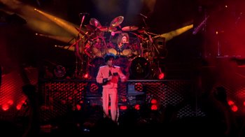 Movie still from “Sign 'o' the Times” (1987), directed by Albert Magnoli – A man standing on top of a stage with a microphone; Wide shot, Overhead angle