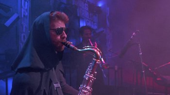 Movie still from “Sign 'o' the Times” (1987), directed by Albert Magnoli – A man playing a saxophone while wearing sunglasses; Medium shot, Low angle