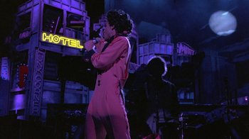 Movie still from “Sign 'o' the Times” (1987), directed by Albert Magnoli – A woman in a pink outfit singing into a microphone; Wide shot, Over the shoulder angle