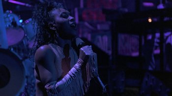 Movie still from “Sign 'o' the Times” (1987), directed by Albert Magnoli – A woman is singing into a microphone in the dark; Medium shot, Low angle
