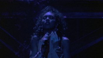 Movie still from “Sign 'o' the Times” (1987), directed by Albert Magnoli – A woman is singing into a microphone in the dark; Close Up shot, Over the shoulder angle