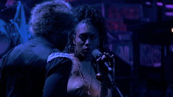 Movie still from “Sign 'o' the Times” (1987), directed by Albert Magnoli – A woman is singing into a microphone in the dark; Close Up shot, Over the shoulder angle