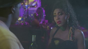 Movie still from “Sign 'o' the Times” (1987), directed by Albert Magnoli – A woman sitting at a table with a bottle of wine in front of her; Close Up shot, Over the shoulder angle