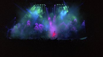 Movie still from “Sign 'o' the Times” (1987), directed by Albert Magnoli – A man playing guitar on a stage in front of an audience; Extreme Wide shot, High angle