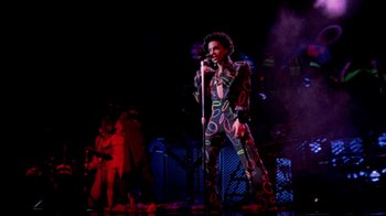 Movie still from “Sign 'o' the Times” (1987), directed by Albert Magnoli – A man in a colorful outfit singing on a stage; Wide shot, Low angle