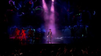 Movie still from “Sign 'o' the Times” (1987), directed by Albert Magnoli – A man standing on a stage in front of an audience; Extreme Wide shot, High angle