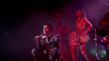 Movie still from “Sign 'o' the Times” (1987), directed by Albert Magnoli – A group of people on a stage singing; Wide shot, Low angle