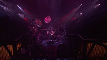 Movie still from “Sign 'o' the Times” (1987), directed by Albert Magnoli – A man is playing drums in front of a crowd; Wide shot, High angle