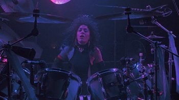 Movie still from “Sign 'o' the Times” (1987), directed by Albert Magnoli – A woman playing drums in a dark room; Medium shot, Low angle