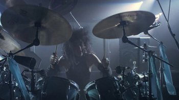 Movie still from “Sign 'o' the Times” (1987), directed by Albert Magnoli – A person playing drums in a dark room; Medium shot, Low angle