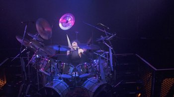Movie still from “Sign 'o' the Times” (1987), directed by Albert Magnoli – A man is playing drums on a stage; Wide shot, High angle