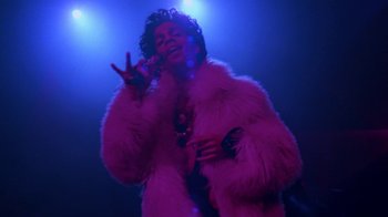 Movie still from “Sign 'o' the Times” (1987), directed by Albert Magnoli – A woman in a pink fur coat singing into a microphone; Medium shot, Low angle
