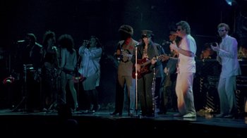 Movie still from “Sign 'o' the Times” (1987), directed by Albert Magnoli – A group of people standing on a stage with guitars; Wide shot, High angle