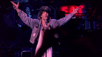 Movie still from “Sign 'o' the Times” (1987), directed by Albert Magnoli – A man in a hat is singing into a microphone; Medium shot, Low angle