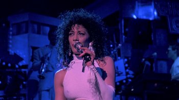 Movie still from “Sign 'o' the Times” (1987), directed by Albert Magnoli – A woman in a white dress singing into a microphone; Close Up shot, Low angle
