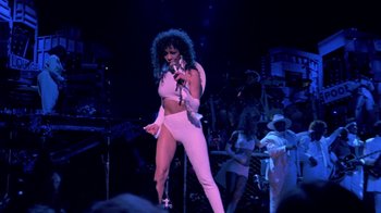 Movie still from “Sign 'o' the Times” (1987), directed by Albert Magnoli – A woman in a white outfit holding a microphone; Wide shot, Low angle