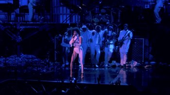 Movie still from “Sign 'o' the Times” (1987), directed by Albert Magnoli – A woman is singing on a stage with a group of people; Wide shot, High angle