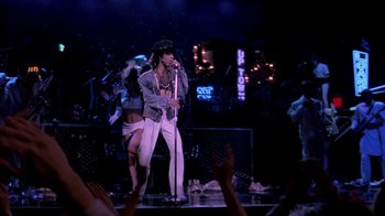 Movie still from “Sign 'o' the Times” (1987), directed by Albert Magnoli – A man is singing on a stage while people clap; Wide shot, Low angle