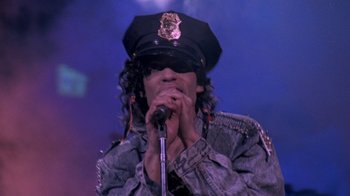 Movie still from “Sign 'o' the Times” (1987), directed by Albert Magnoli – A man in a black hat is singing into a microphone; Close Up shot, Low angle