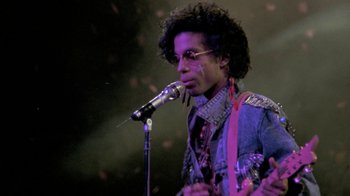 Movie still from “Sign 'o' the Times” (1987), directed by Albert Magnoli – A man with a microphone in front of a microphone stand; Medium shot, Low angle