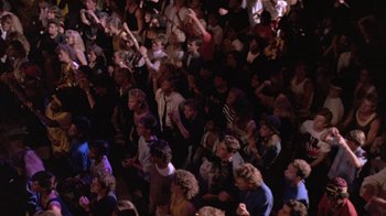 Movie still from “Sign 'o' the Times” (1987), directed by Albert Magnoli – A crowd of people standing in a dark room; Wide shot, High angle