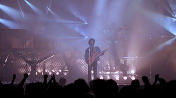 Movie still from “Sign 'o' the Times” (1987), directed by Albert Magnoli – A man with a guitar on stage in front of an audience; Wide shot, Low angle