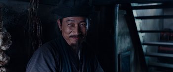Movie still from “Silence” (2016), directed by Martin Scorsese – A man wearing a hat and a black jacket; Close Up shot, Over the shoulder angle