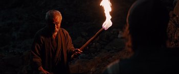 Movie still from “Silence” (2016), directed by Martin Scorsese – An old man holding a burning stick in his hand; Medium shot, Over the shoulder angle