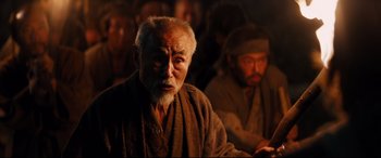 Movie still from “Silence” (2016), directed by Martin Scorsese – An old man with a gray beard is sitting next to another old man; Medium shot, Over the shoulder angle