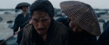 Movie still from “Silence” (2016), directed by Martin Scorsese – A man with a hat is standing next to another man; Close Up shot, Over the shoulder angle