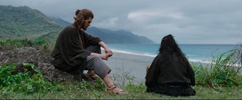 Movie still from “Silence” (2016), directed by Martin Scorsese – A man and a woman sitting on the grass near the ocean; Medium shot, Over the shoulder angle