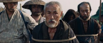 Movie still from “Silence” (2016), directed by Martin Scorsese – An old man tied up with a rope in front of a group of people; Close Up shot, Over the shoulder angle
