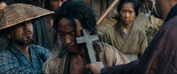 Movie still from “Silence” (2016), directed by Martin Scorsese – A man holding a wooden cross in front of a crowd; Close Up shot, High angle