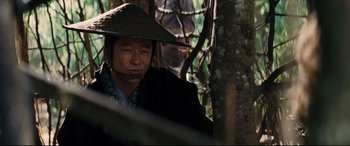 Movie still from “Silence” (2016), directed by Martin Scorsese – A man wearing a hat sitting next to a tree; Close Up shot, Over the shoulder angle